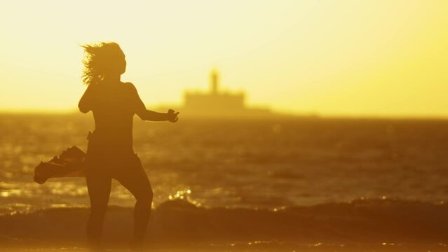 Silhouette of a graceful young woman in a dress dancing on the seashore at bright orange sunset