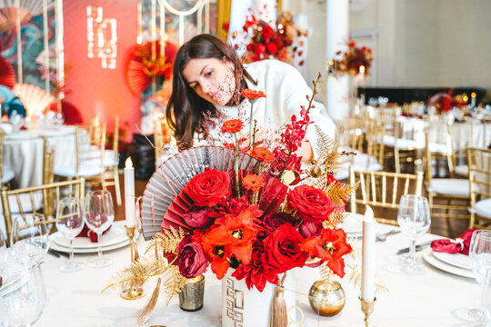 Red gold color flower decor for Chinese New Year celebration. Girl woman florist, decorator, organizer of events, parties, wedding planner making floral arrangement, festive bouquet, table decoration