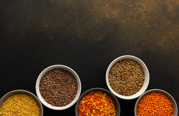 Multicolored lentils in bowls on a brown background, yellow and brown, green and orange lentils, healthy legumes, top view, copy space