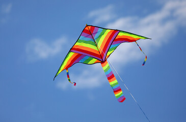 Colorful toy kite with rainbow hues flies tied on a string in the sky