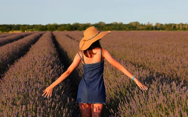 Fotobehang woman in denim dress and straw hat looking at lavender flower field at sunset © ChiccoDodiFC