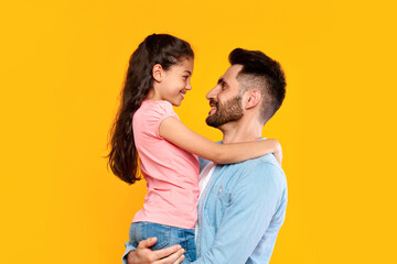 Father's love. Loving father holding his little daughter, dad bonding with her child girl, yellow background, side view