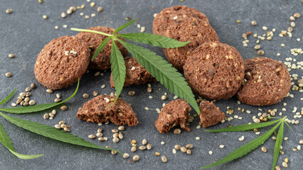 Cannabis leaves and baked chocolate cookies infused  crushed hemp seeds and cbd oil closeup on  dark grey stone table. Sweet dessert with cannabis products ingredients