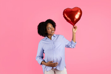 Positive millennial black pregnant lady touching big belly, hold heart shaped inflatable balloon,...