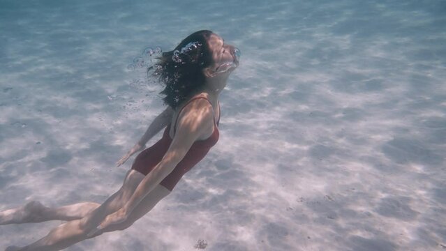 Underwater girl swimming in the crystal clear water, wearing red swimsuit, clear emerald sea