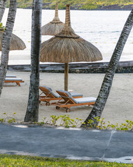 sun loungers with mat, table, cushions, umbrella and towels in a luxury resort in mauritius. In the background you can see palm trees, the beach and the ocean. Chopped plane.