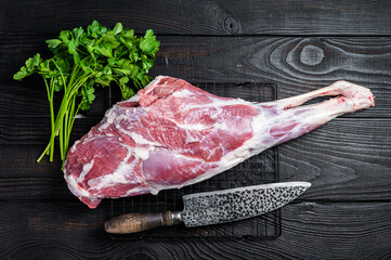 Fresh Raw whole lamb mutton leg thigh on kitchen table with herbs. Black Wooden background. Top view - obrazy, fototapety, plakaty