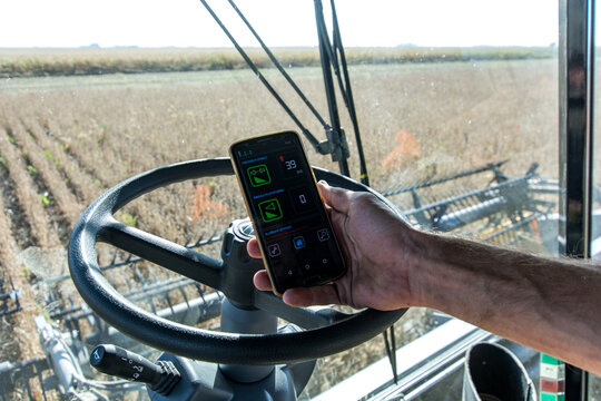 Mano sosteniendo un celular con aplicaci&oacute;n para manejar trilladora de granos desde arriba del tractor