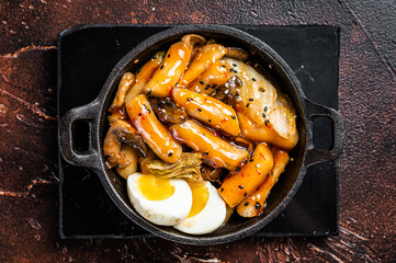 Korean Topokki or Tteokbokki rice cake with egg and mashrooms. Dark background. Top view