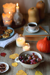 Obraz na płótnie Canvas Cup of tea or coffee, plate with desserts, dried oranges, bowl of grapes, scented candles, vintage books, pumpkins and autumn leaves on the table. Autumnal hygge. Selective focus.