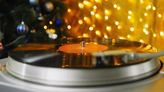 Retro turntable with vinyl records and a needle on the background of Christmas lights spins the record. Medium plan.