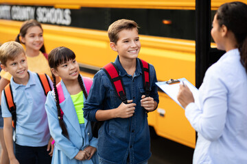 Happy schoolchildren waiting to get on school bus, standing in turn