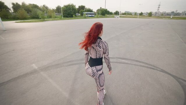 Slim Woman with Red Hair in Sports Overalls is Rollerblading. Beautiful Happy Girl with a Slender Figure and in Tight Clothes Roller-Skates. Slow Motion.