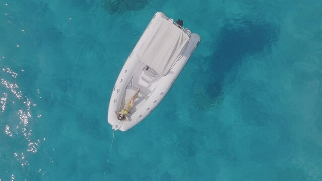 Girl sunbathing on a boat in the crystal clear sea, aerial top down view, Sardinia, Italy