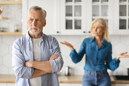 Upset mature man with arms crossed having quarrel with wife in kitchen