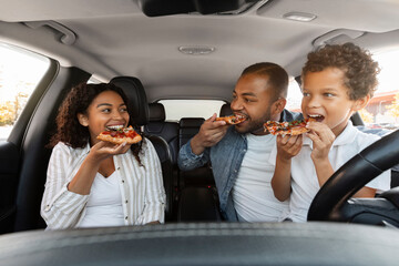 Cute african american family sitting in car, eating pizza