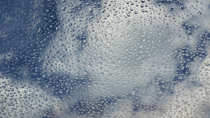 Raindrops on the glass on the background of a blue cloudy sky.