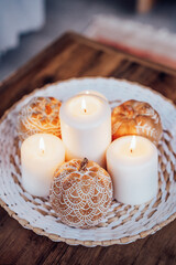 Close up autumn fall cozy mood composition for hygge home decor. Orange pumpkins decorated with mandalas, white burning candles on wicker plate on the coffee table. Selective focus. Vertical card.