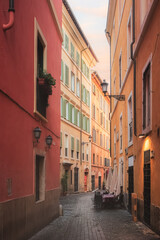 Bright, colourful residential buildings and architecture along a quiet, narrow cobblestone lane in Rione VI Parione in the old town of historic central Rome, Italy.