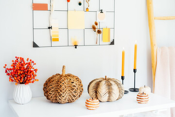 Cozy autumn home interior decor- various decorative wicker pumpkins, candles, seasonal flowers in vase on the white table with mood board with fall colors palette notes on the wall. Mood inspiration