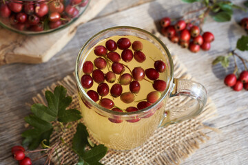 A cup of herbal tea with fresh hawthorn berries on a table
