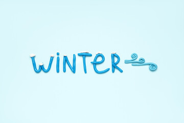 Word WINTER made of play dough on light blue background