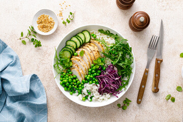 Chicken meat and rice lunch bowl with green peas, red cabbage, cucumber and fresh arugula salad