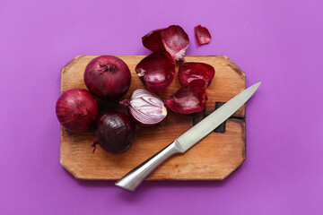 Wooden board with fresh red onions on purple background