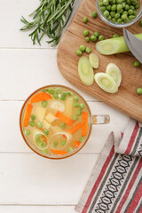 Glass cup of tasty vegetable broth on white wooden background