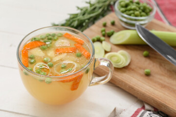 Glass cup of tasty vegetable broth on white wooden background