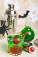 Glass of delicious cocktail for Halloween with tasty cherry, measure cup and candy on light background, closeup