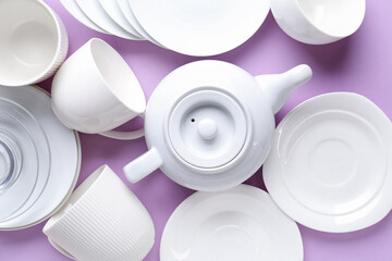Many porcelain teapots and cups on lilac background