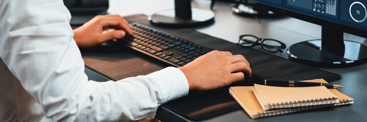 Office worker sitting on workspace desk, focused and engaged, using computer and typing on keyboard to input data ensure accurate data management in the modern workplace. Trailblazing