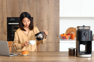 Beautiful Asian woman pouring coffee into cup in kitchen
