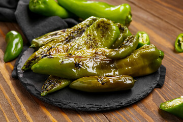 Slate board with grilled chili peppers on wooden background