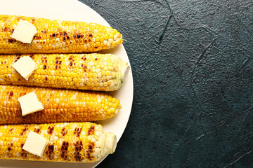 Plate of tasty grilled corn cobs with butter on dark background