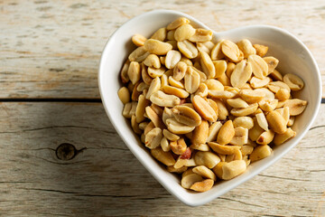 top view of a heart-shaped container with shelled and salted roasted peanuts