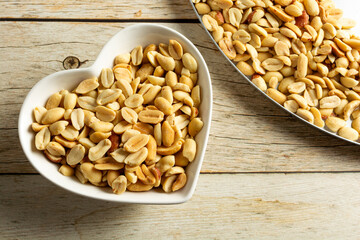 top view of a heart-shaped container with shelled and salted roasted peanuts