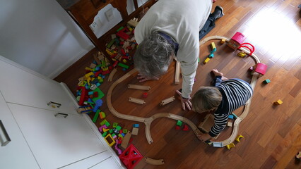 Little boy building train tracks with the help of his grandfather, seen from above perspective....