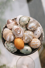 Beautifully decorated chicken eggs for Easter. Easter eggs decorated with rhinestones and shiny stones. A pile of differently decorated Easter eggs lie in a dish on the background of the lawn