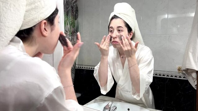 Young woman looking in mirror while applying beauty product at home