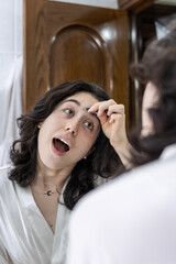 Fototapeta premium Young woman looking in the mirror in the morning. Woman in nightwear looking in the mirror in the morning