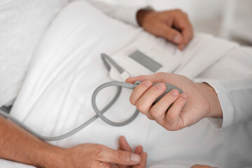 Male nurse measuring blood pressure of senior man in bedroom, closeup