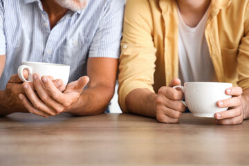Senior man with his son drinking tea in kitchen, closeup