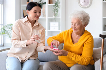 Senior woman with her daughter taking pills at home - obrazy, fototapety, plakaty
