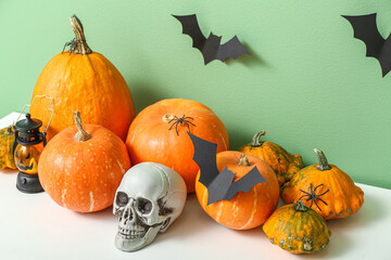 Halloween pumpkins with skull and paper bats on commode near green wall, closeup