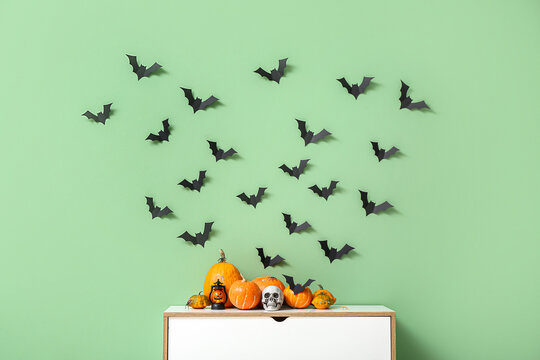 Halloween pumpkins with skull and paper bats on commode near green wall