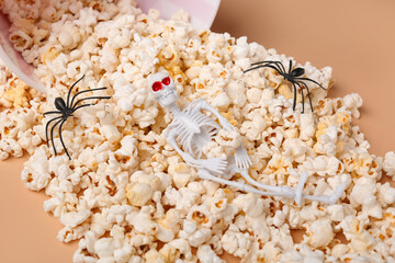 Bucket with tasty popcorn, spiders and skeleton for Halloween celebration on beige background, closeup