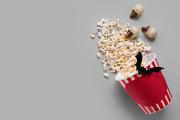 Bucket with tasty popcorn, skulls and paper bat for Halloween celebration on grey background