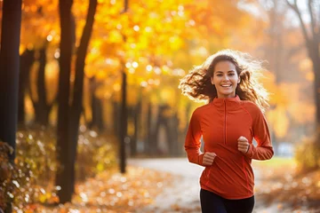 Poster Happy female runner jogging on a park on an autumn day © MVProductions